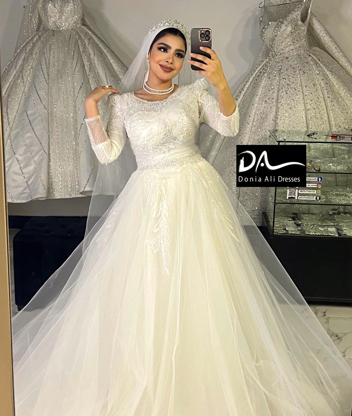 فستان عروسه طويل منفوش من التول أبيض بصدر مطرز بالترتر والخرز اللامع بطرحه تل و بأكمام طويلة